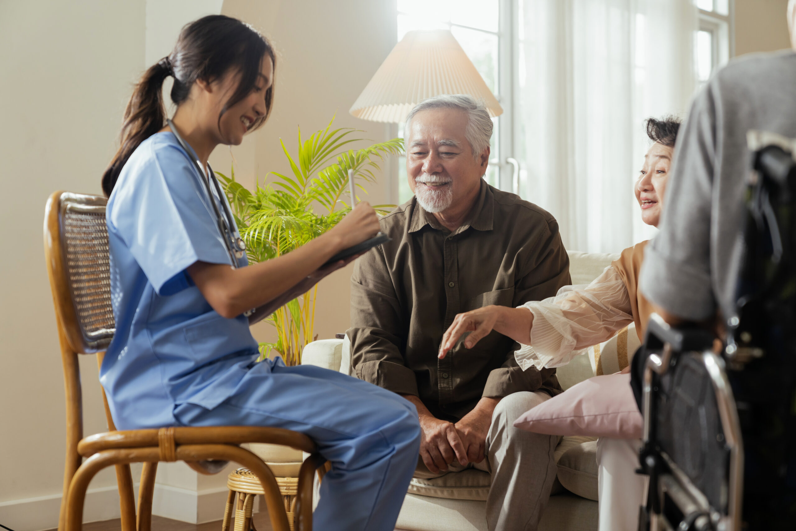happiness-cheerful-elderly-woman-men-talking-with-female-caregiver-nurse-doctor-having-health-checking-consult-living-areacaretakers-with-senior-couple-sitting-living-room-nursing-home