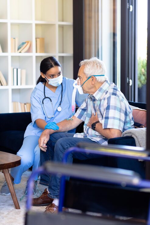 biracial-female-health-worker-helping-caucasian-senior-man-use-oxygen-mask-home_13339-334188