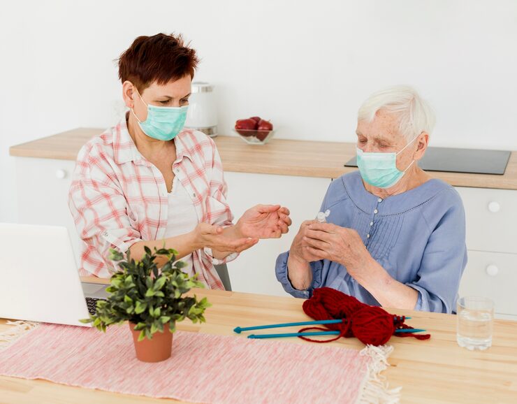 elder-women-with-medical-masks-disinfecting-their-hands-while-knitting_23-2148492279