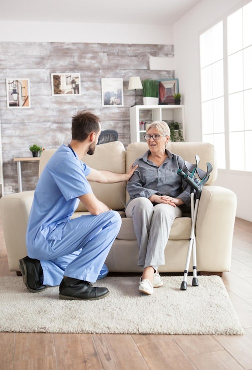 male-health-visitor-nursing-home-talking-with-retired-old-woman-while-sitting-couch-old-woman-with-crutches_482257-45110